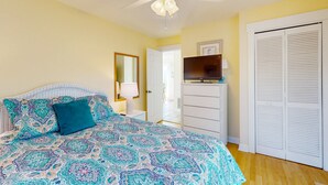 A bedroom with a patterned bedspread, a ceiling fan, a TV on a dresser, and a wardrobe.