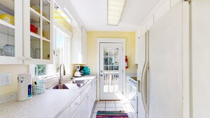 A narrow kitchen with white cabinets, a stainless steel sink, a colorful rug, and a door leading to a balcony.