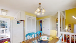 A dining area with a glass table, blue chairs, a white refrigerator, and a chandelier.