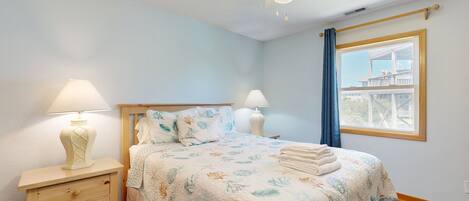 A bedroom with a bed, two bedside lamps, a ceiling fan, a window with a view, and a wooden nightstand with drawers.