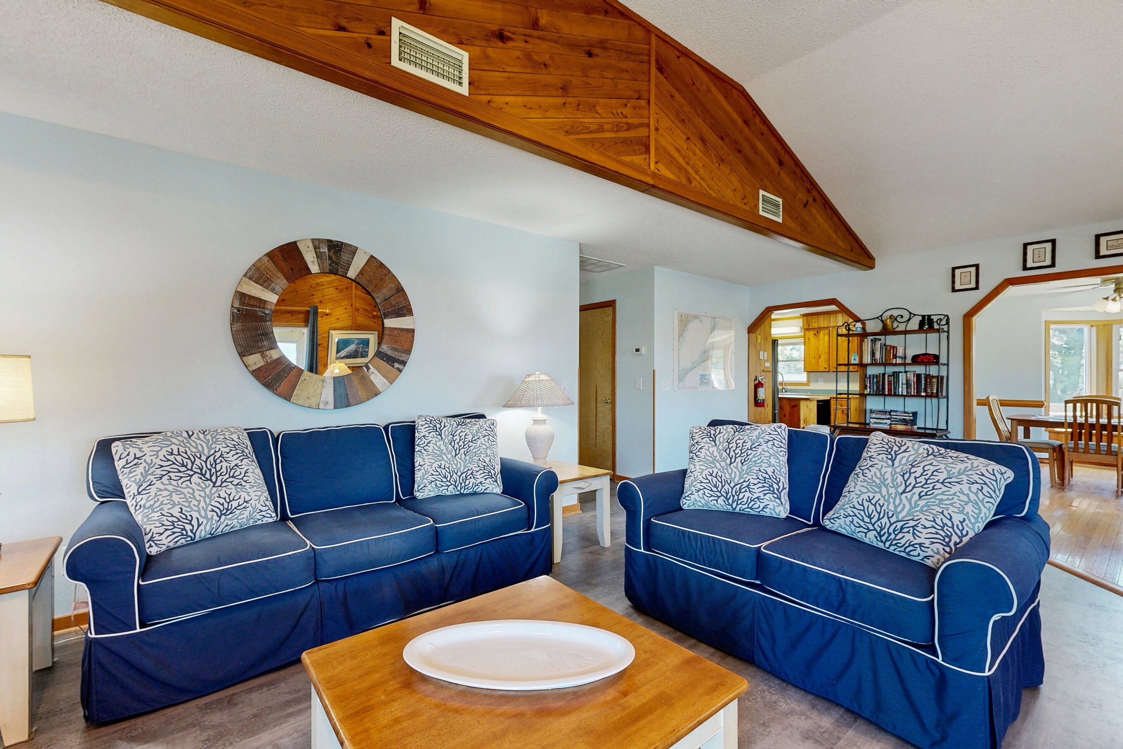 Un salon avec deux canapés bleus, une table basse en bois et un grand miroir rond accroché au mur.