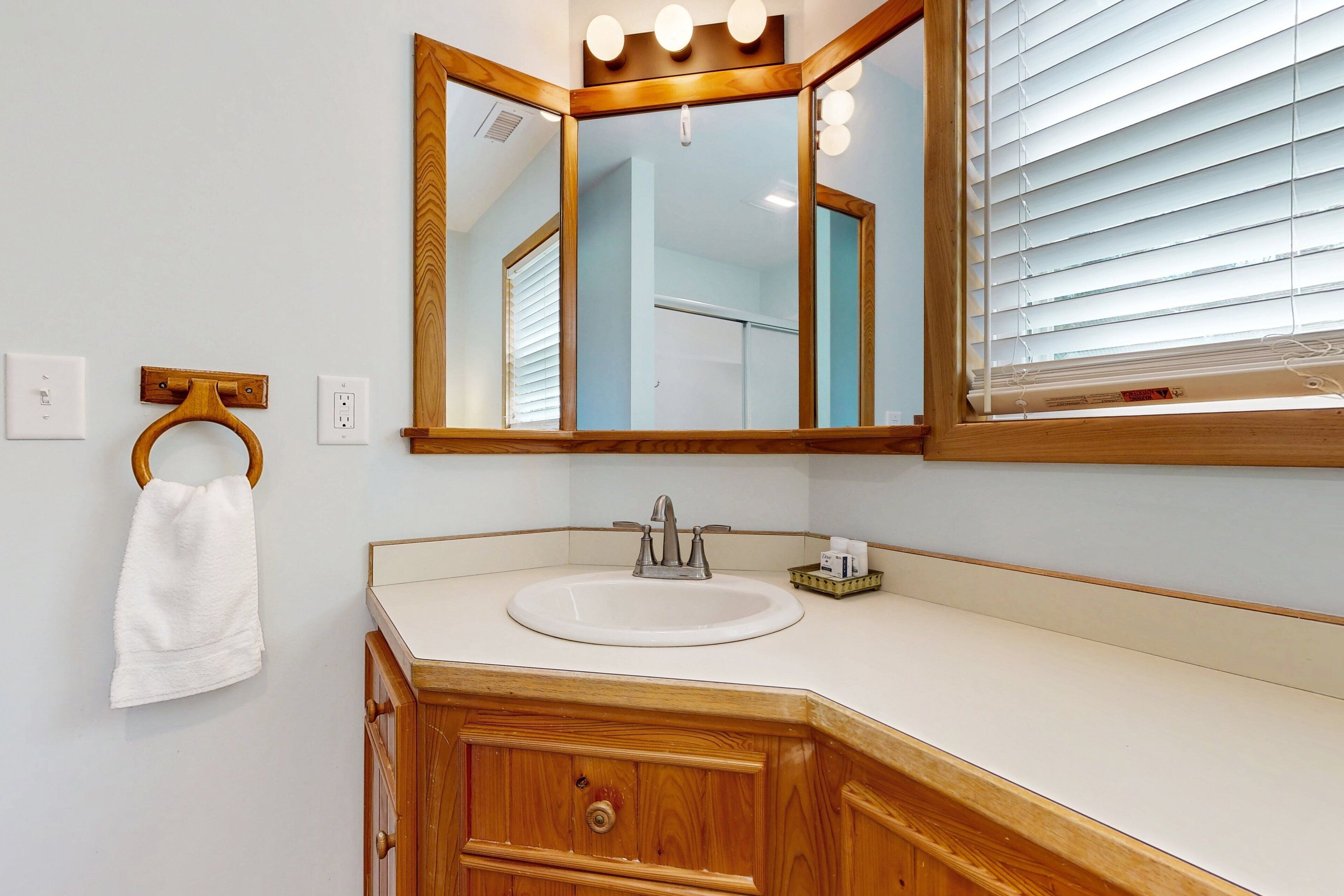Un baño con tocador de madera, lavamanos blanco, espejo con iluminación y perchero para toallas.