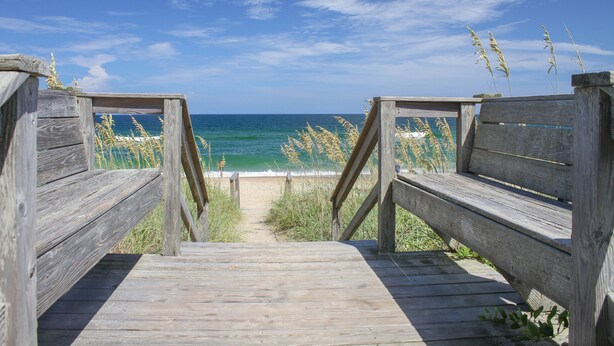 Une promenade en bois qui mène à une plage d’où l’on a une vue dégagée sur l’océan.