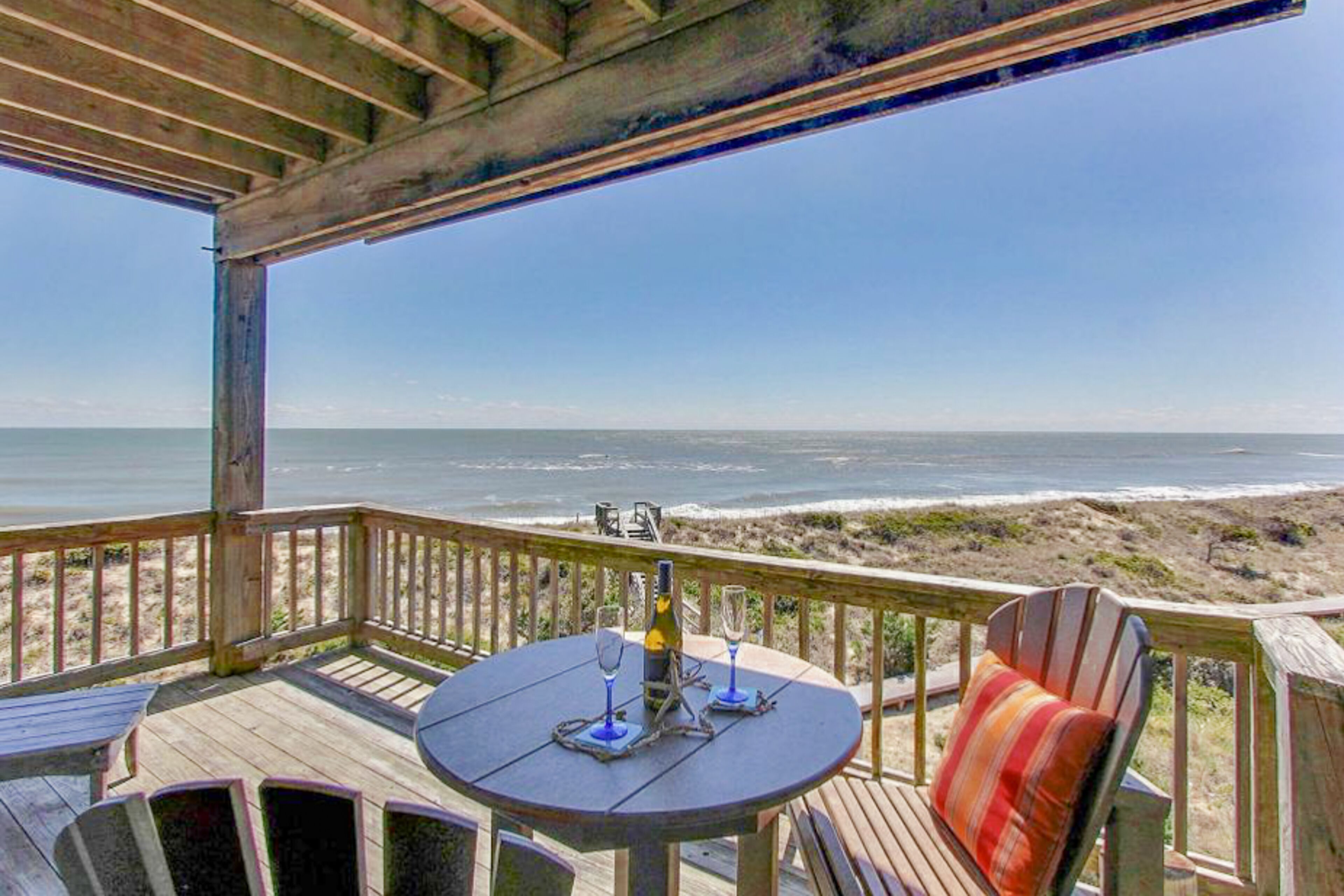 Une terrasse en bois avec une table et des chaises, donnant sur une plage.