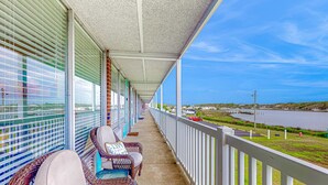 A covered balcony with wicker chairs and a view of a lake and distant buildings. - Sea Alcove: Colorful studio near the ocean with pool & kitchenette (Atlantic Beach)
