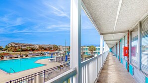 A hotel corridor with a pool area, featuring a long balcony with a view of the pool and adjacent buildings. - Sea Alcove: Colorful studio near the ocean with pool & kitchenette (Atlantic Beach)
