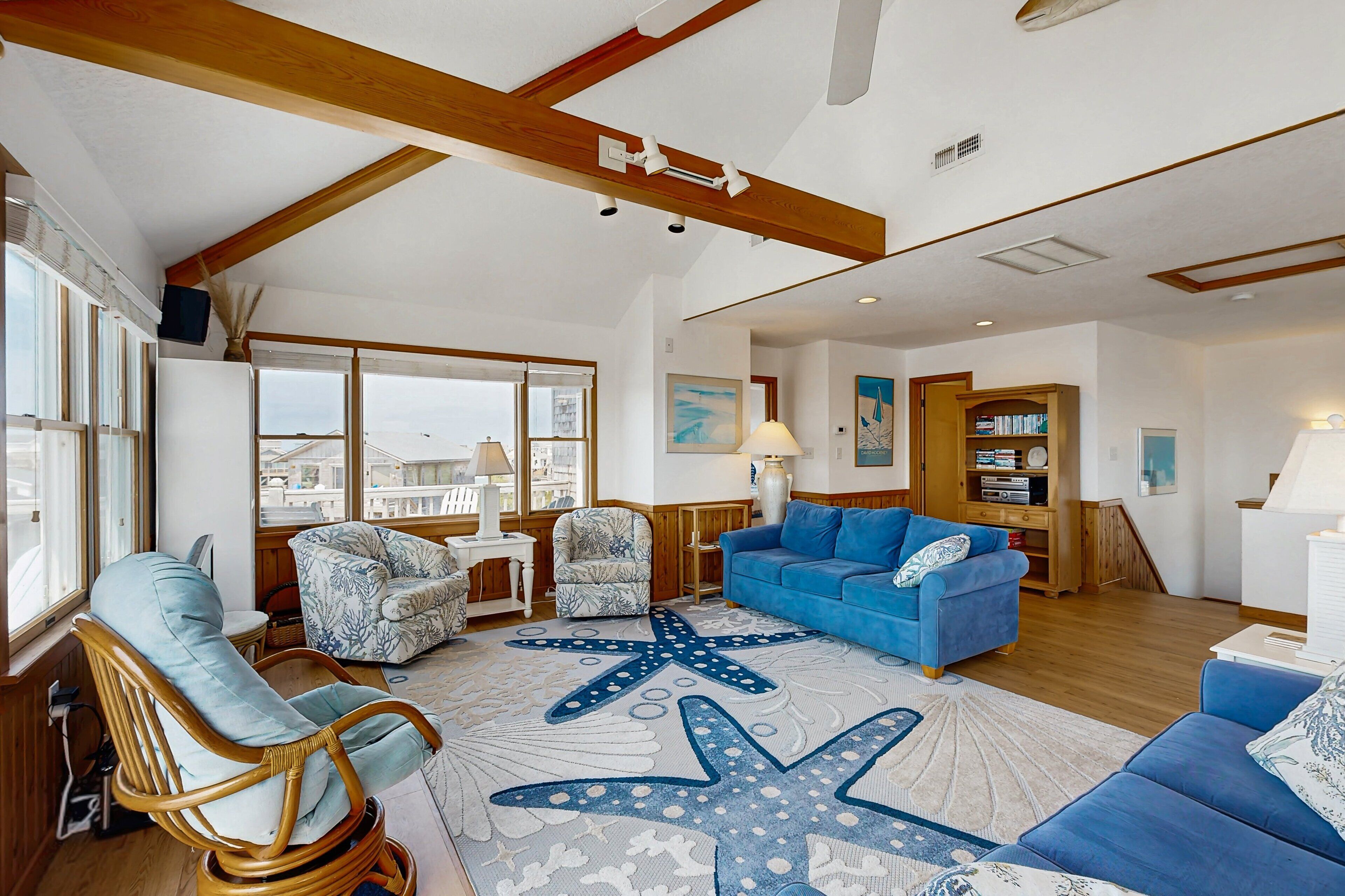 A spacious living room with a large starfish rug, a blue sofa, and a wicker chair.