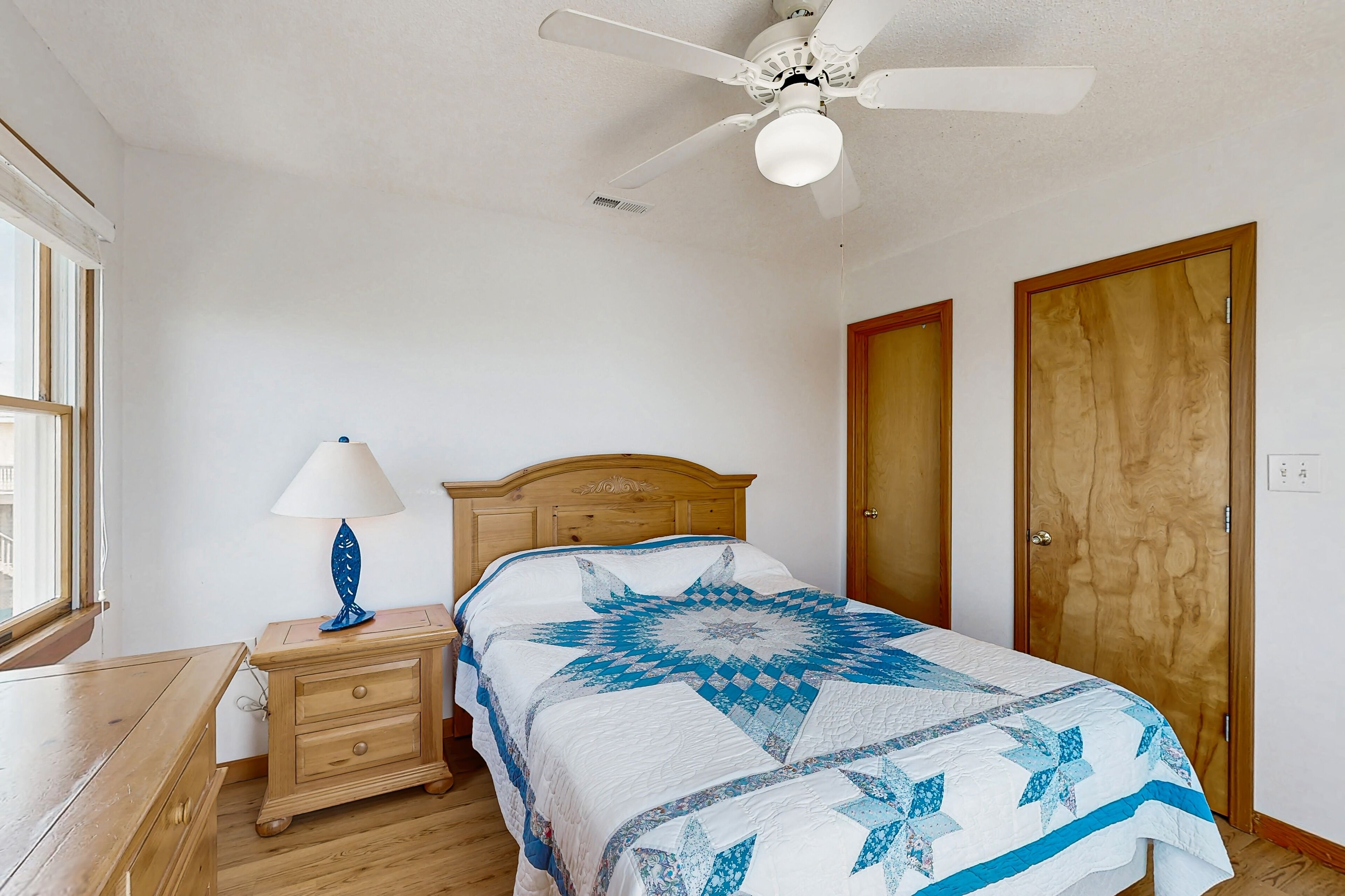 A bedroom with a wooden bed, a nightstand with a lamp, a ceiling fan, and two wooden doors.
