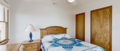A bedroom with a wooden bed, a nightstand with a lamp, a ceiling fan, and two wooden doors.