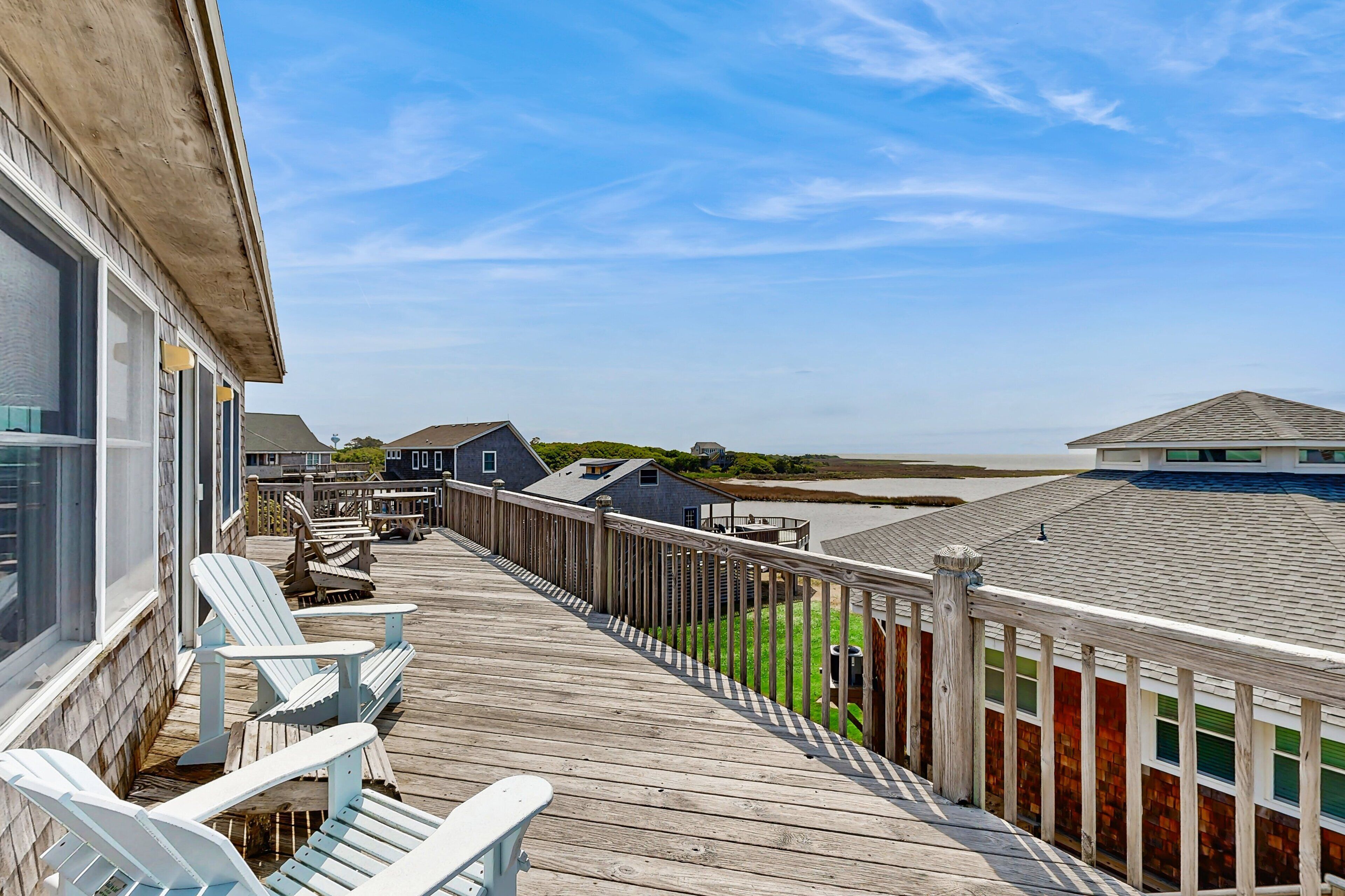 A wooden deck with Adirondack chairs, a view of the beach, and a wooden fence.