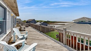 Een houten terras met Adirondack-stoelen, uitzicht op het strand en een houten omheining.