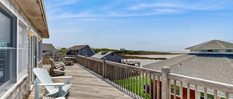 A wooden deck with Adirondack chairs, a view of the beach, and a wooden fence.