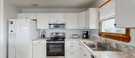 Cocina compacta con armarios blancos, refrigerador de acero inoxidable, horno empotrado, microondas, tostadora y lavaplatos con ventana arriba.