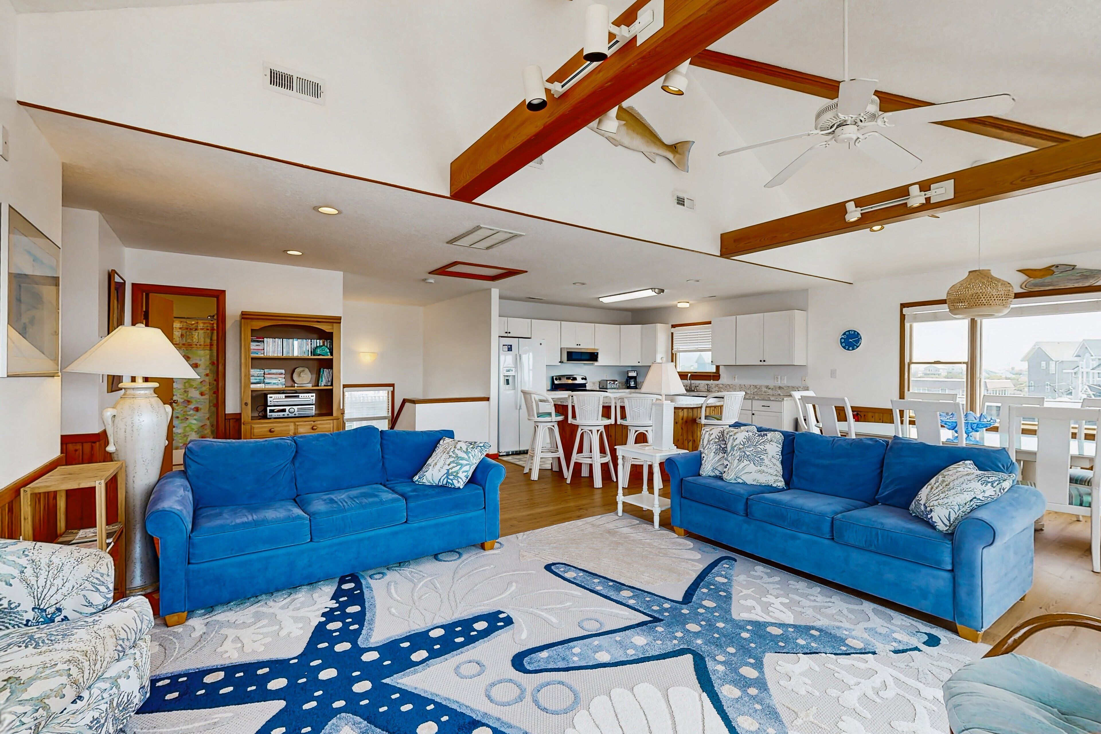 A spacious living room with two blue sofas, a large starfish-patterned rug, and a ceiling fan.