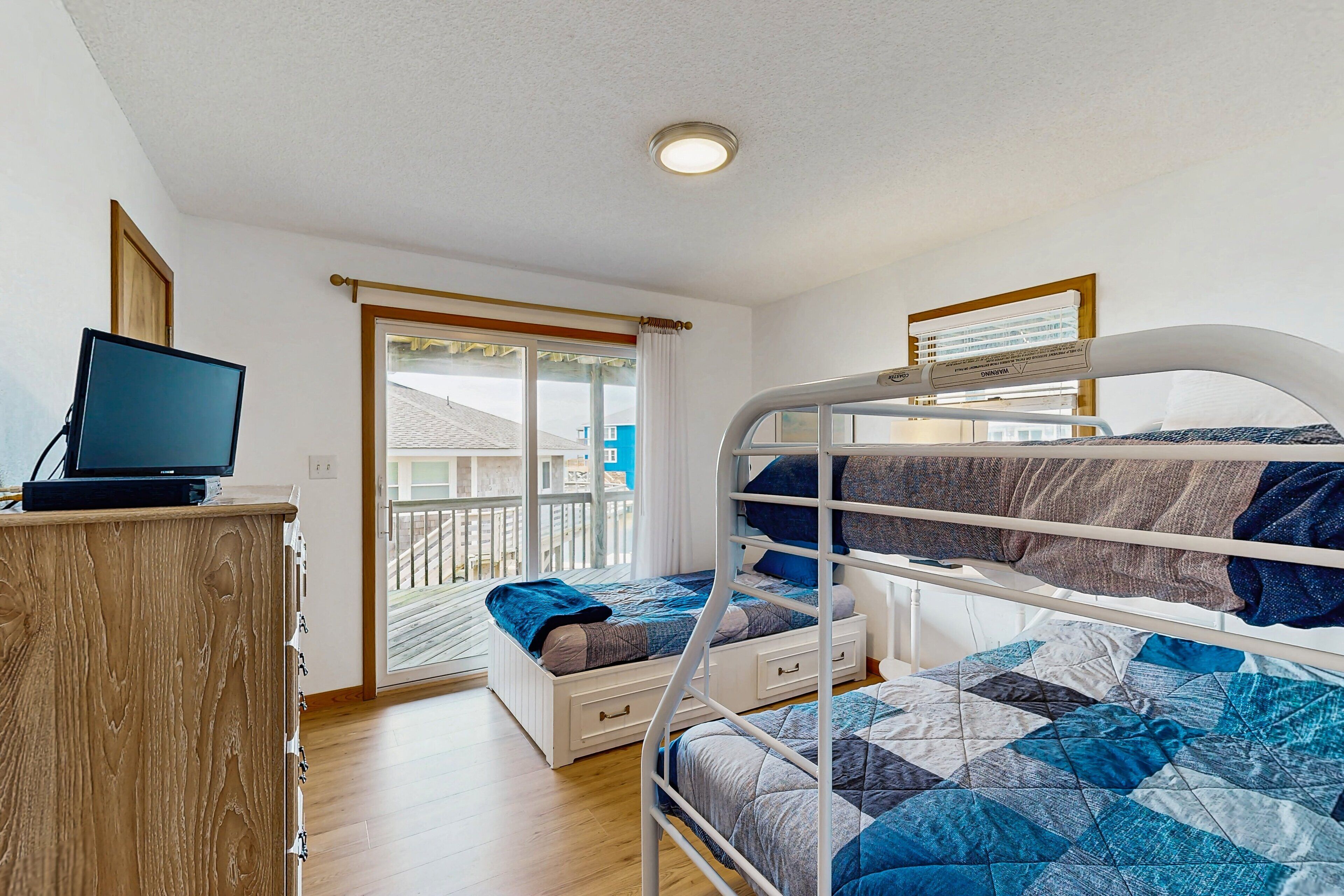 A bedroom with bunk beds, a desk with a computer, and a window with a view of a balcony.