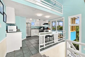 A kitchen with white cabinets, a stainless steel refrigerator, and a dining area with a table and chairs. - Oceanfront Community Pool, New Owners, Newly Renovated, and dog friendly (Avon)