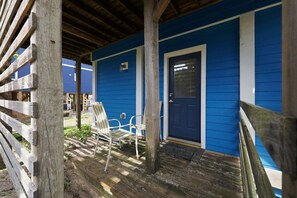 Une véranda en bois avec un mur extérieur bleu, une porte et deux chaises.