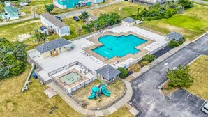 Vista aérea de una zona residencial con piscina, parque infantil y aparcamiento.