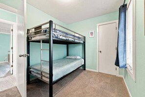 A bunk bed room with a door, a framed picture on the wall, and a window with a curtain.