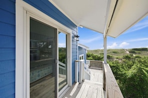 A blue building with a wooden deck, a glass door, and a view of a green landscape. - Oceanfront Community Pool, New Owners, Newly Renovated, and dog friendly (Avon)