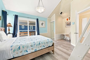 A bedroom with a bed, a nightstand, a lamp, a chair, and a door leading to another room. - Oceanfront Community Pool, New Owners, Newly Renovated, and dog friendly (Avon)