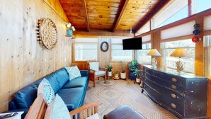 Een gezellig cabin interieur met een houten plafond, een blauwe bank, een houten dressoir en een televisie aan de muur.