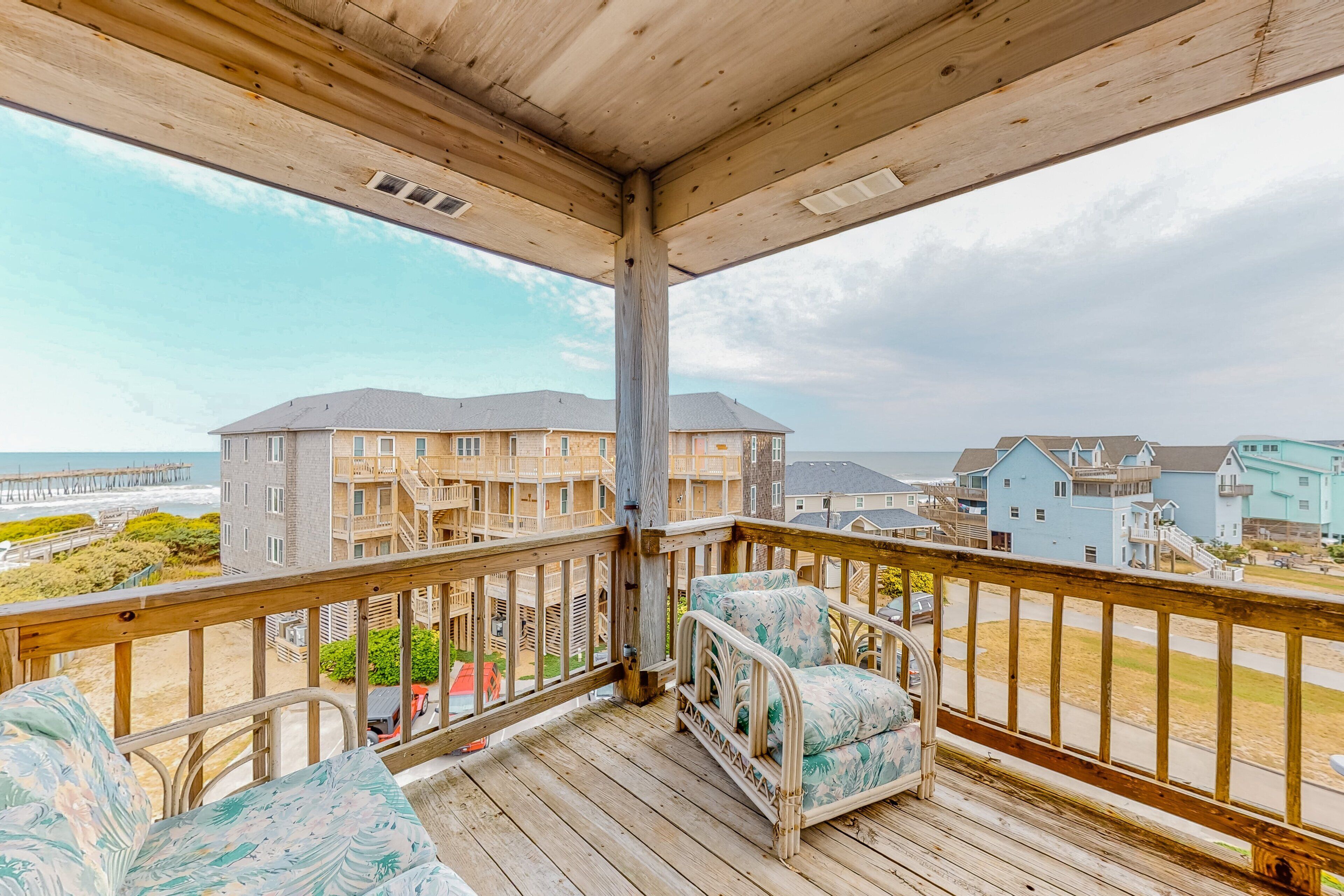 A wooden balcony with a view of a beach and buildings.