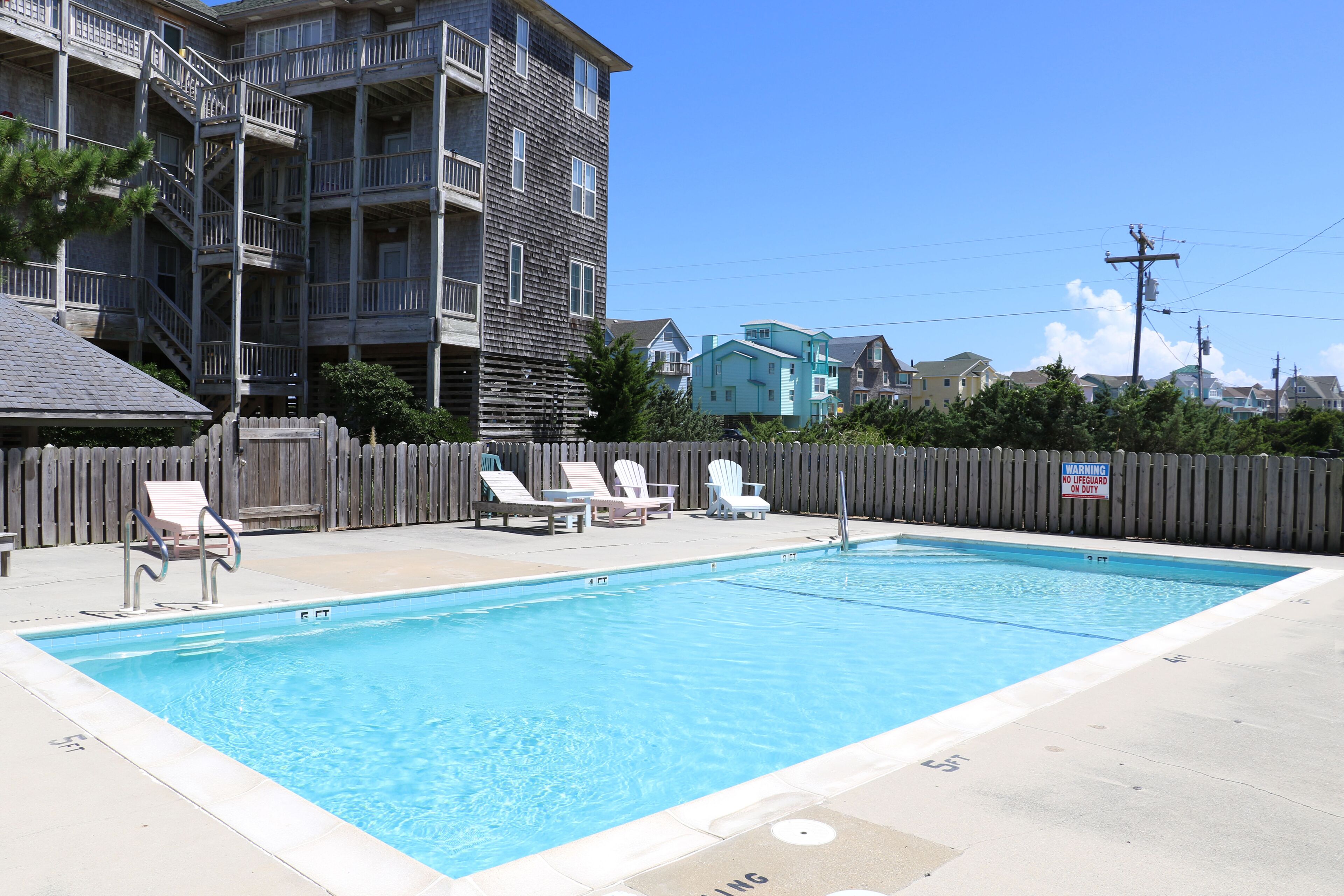 A rectangular swimming pool with a wooden deck and lounge chairs.
