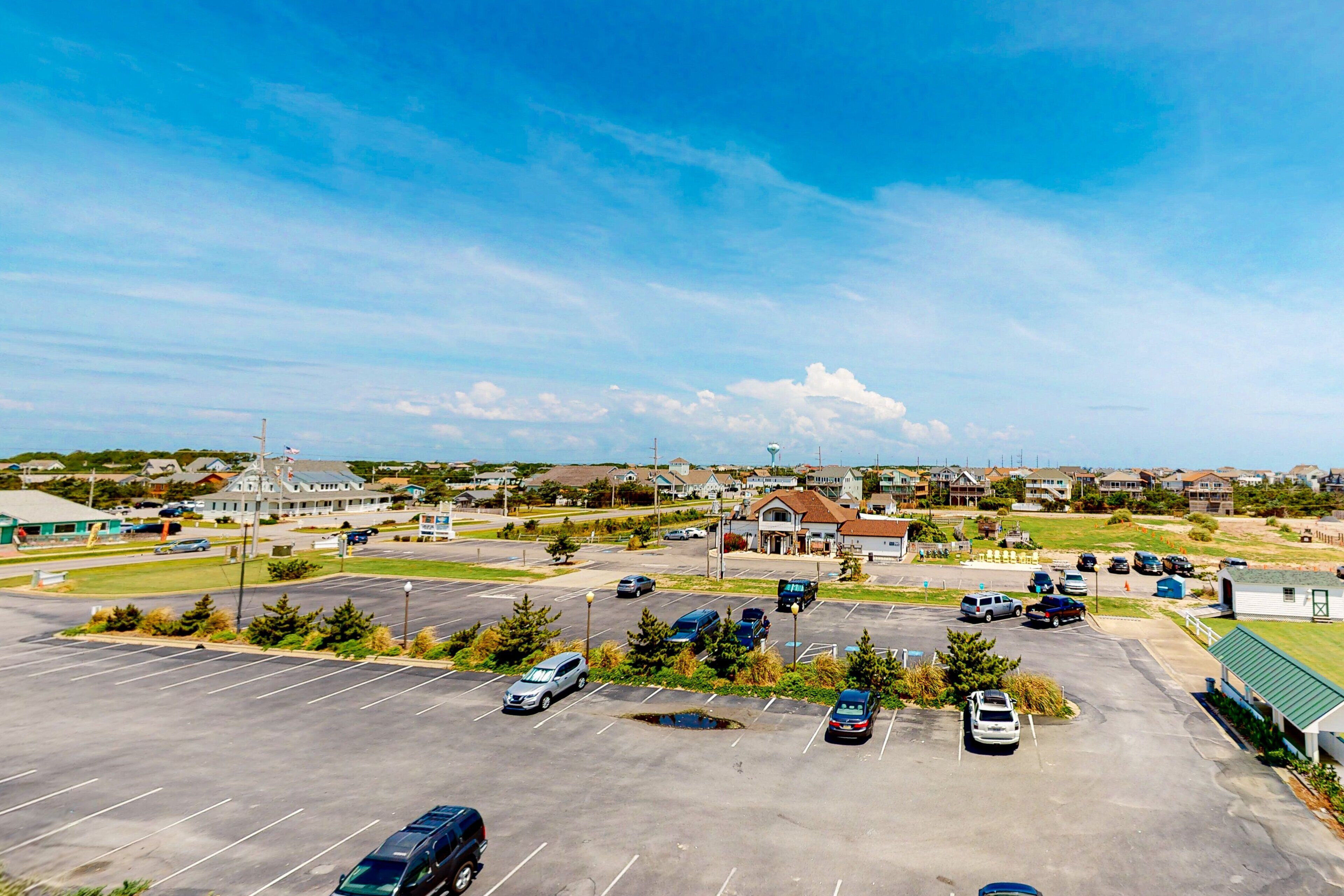 Un parking avec plusieurs voitures, un bâtiment doté d’un toit végétalisé et un ciel bleu dégagé.