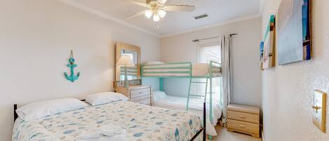 Une chambre comprenant un lit superposé, un lit simple, un ventilateur de plafond, une table de chevet avec une lampe et une petite commode.