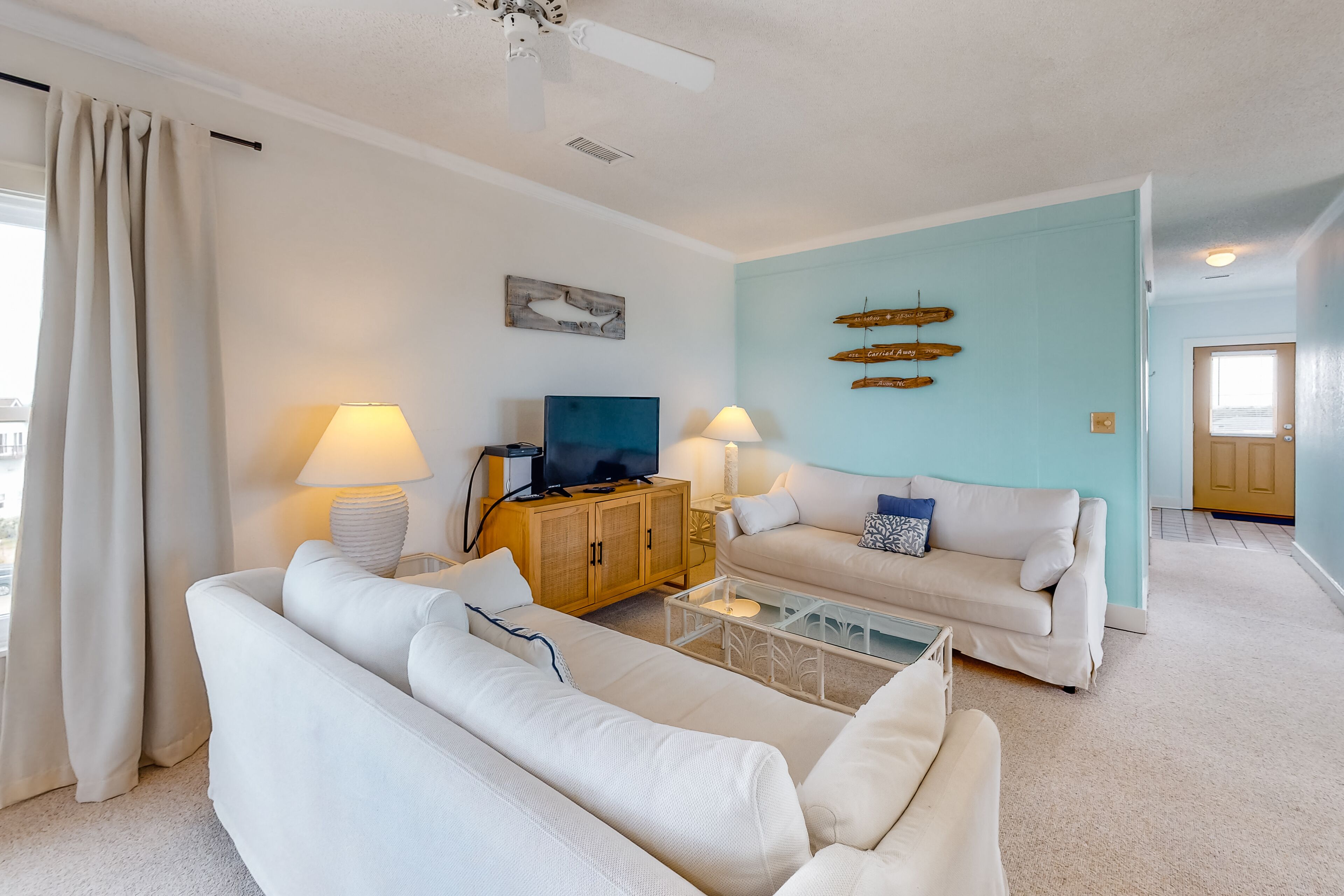 A living room with a sofa, a coffee table, a TV, and a cabinet. There are two lamps, a ceiling fan, and a wall with directional signs.
