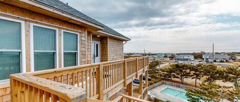 A wooden deck with a pool, a view of the beach, and a cloudy sky.