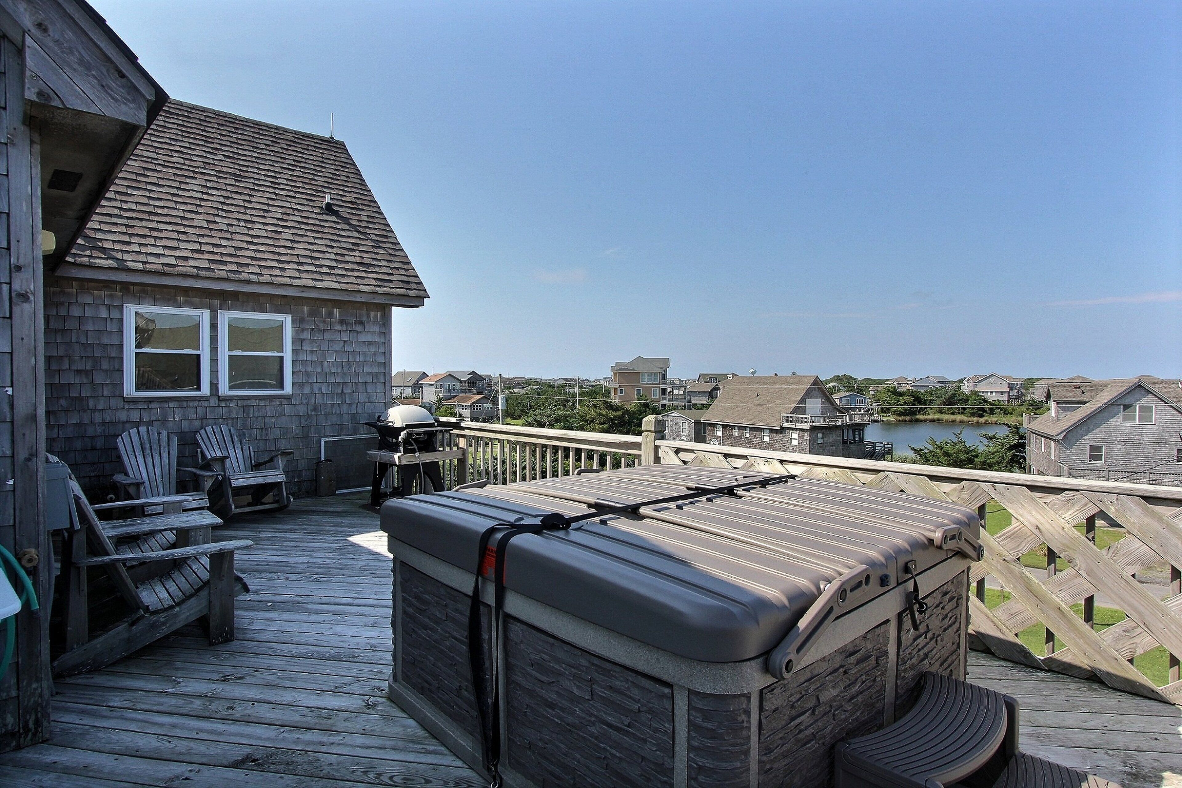 Une terrasse en bois avec des fauteuils Adirondack, un jacuzzi et une vue sur les maisons de l’autre côté de l’étendue d’eau.
