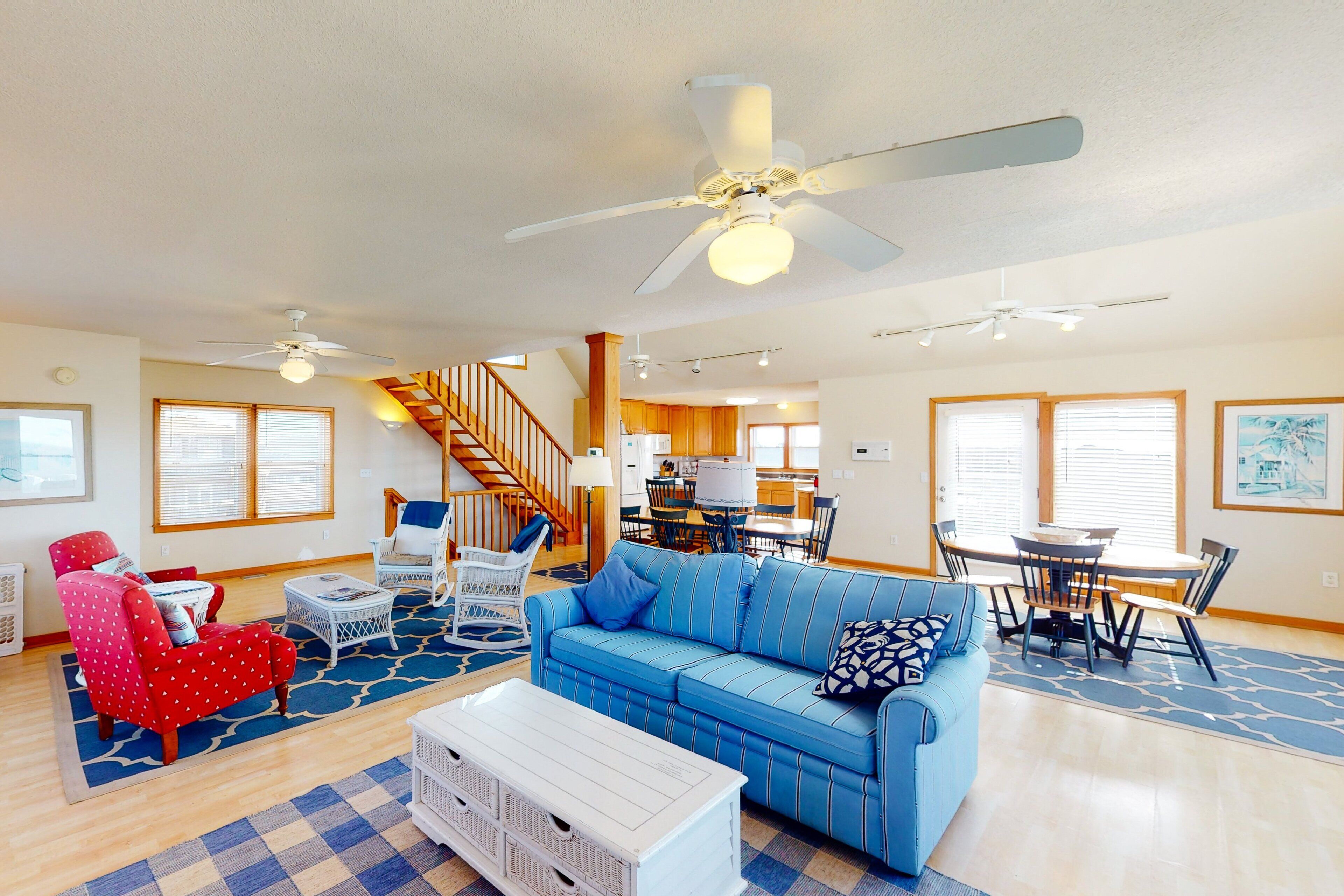A spacious living room with a blue sofa, a red armchair, a white coffee table, and a staircase leading to the upper floor.