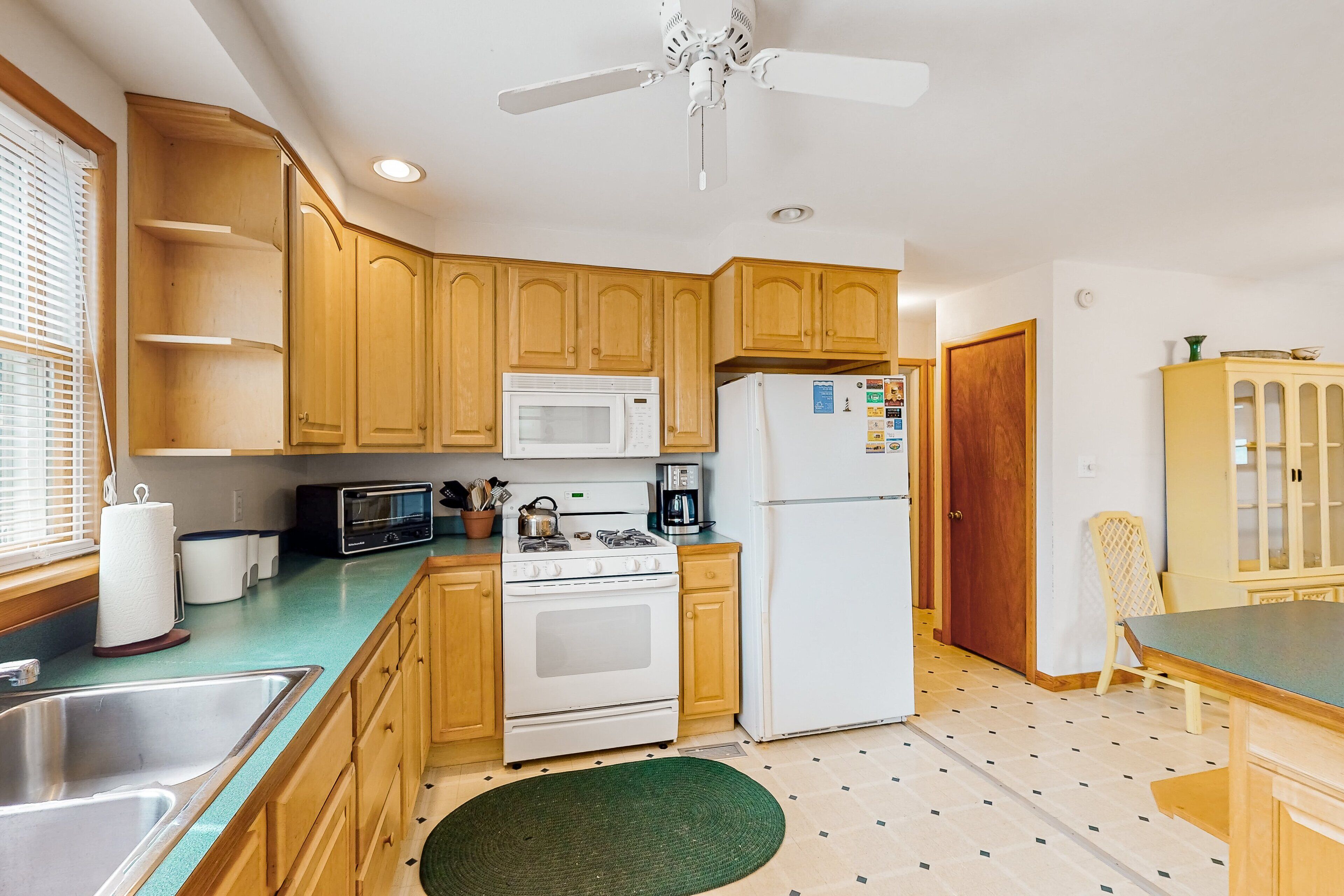 A kitchen with wooden cabinets, a microwave, a stove, a refrigerator, and a ceiling fan.