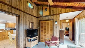 Ein Zimmer mit Holzwänden, einem Fernseher auf einem Holzständer, einem roten Sessel und einem blumigen Sofa.