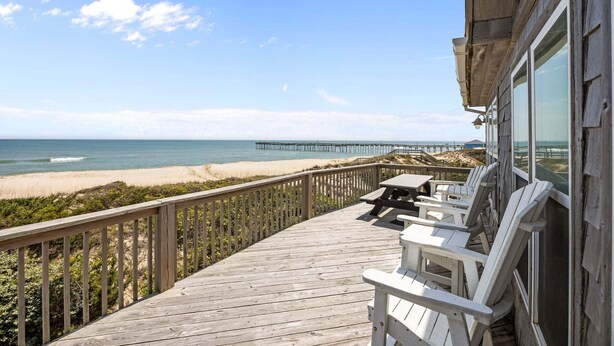 A wooden deck with outdoor seating, overlooking a beach and a pier. - Oceanfront house with private pool, hot tub, & washer/dryer (Avon)
