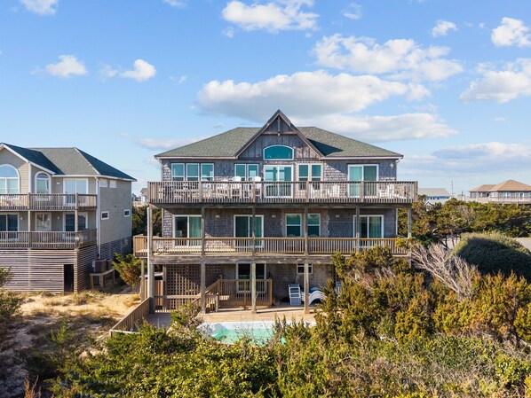A multi-story beachfront house with a pool, balconies, and a view of the ocean.