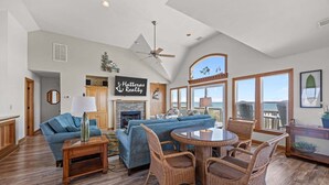A spacious living area with a fireplace, blue sofas, wicker chairs, and large windows offering a view. - Oceanfront house with private pool, hot tub, & washer/dryer (Avon)