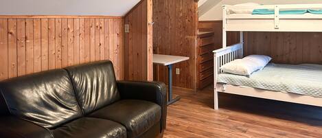 A room with a wooden floor, a black leather sofa, a bunk bed, and a desk.