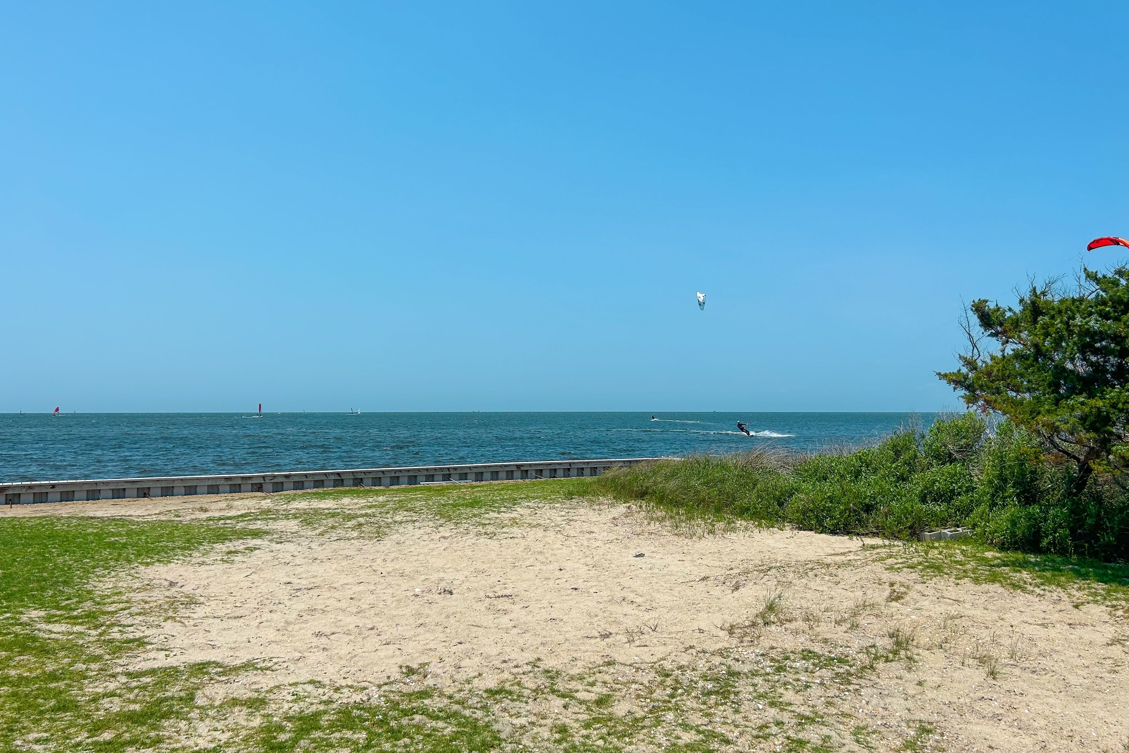 Uma praia com areal arenoso, zona ajardinada e vista para o mar.