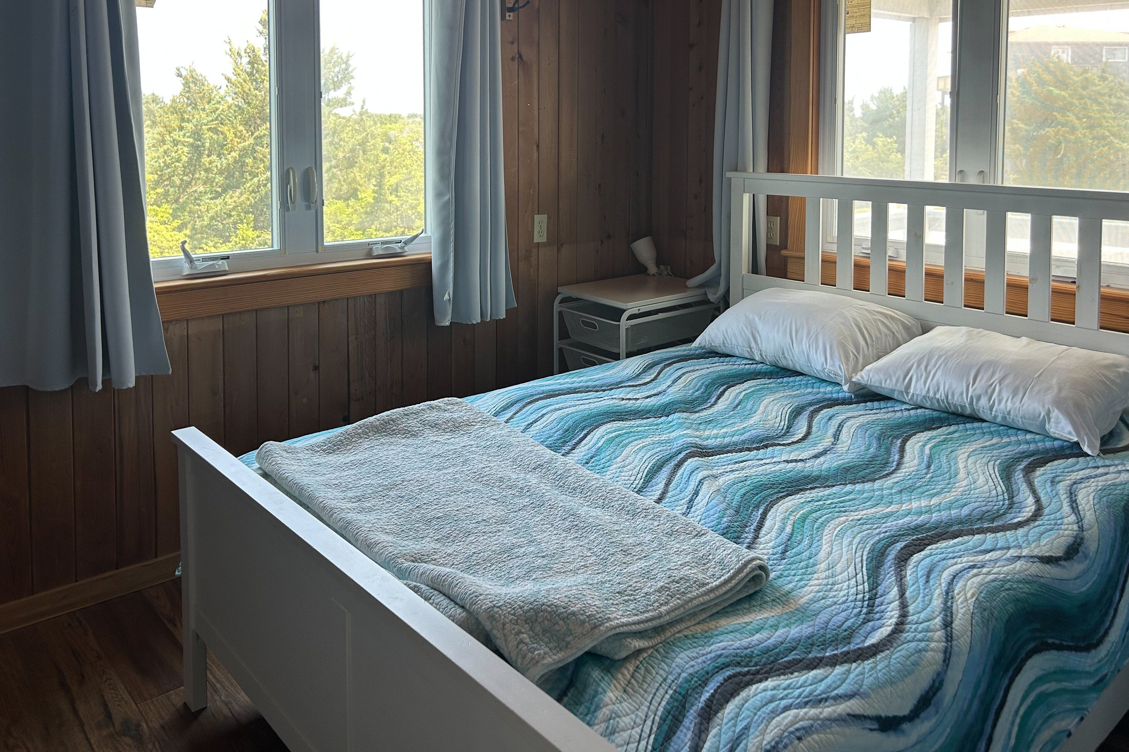Un dormitorio con cama, mesita de noche y ventana con cortinas.