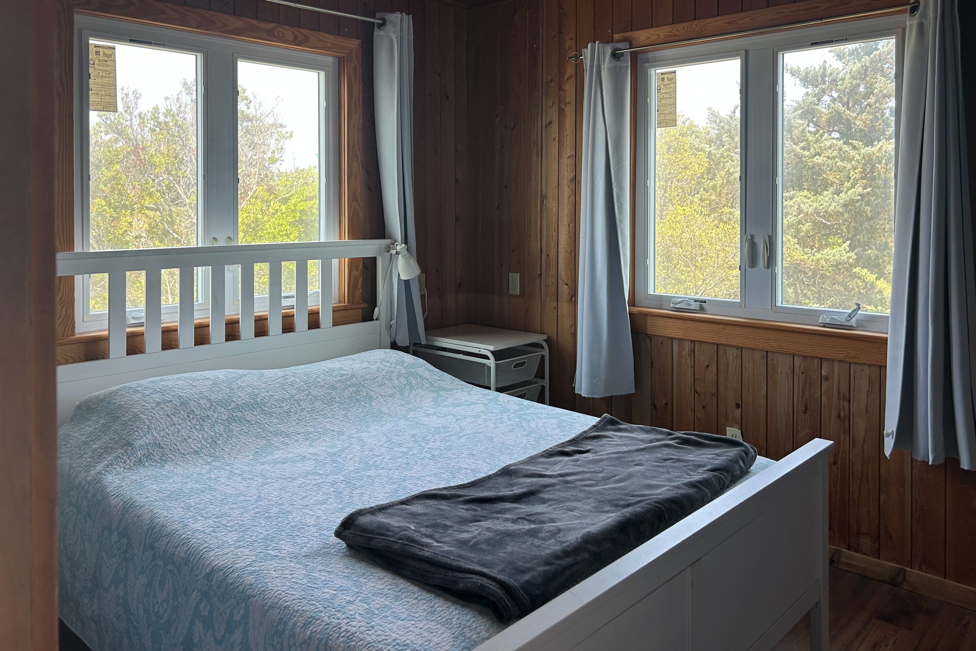 Une chambre à coucher avec un lit, une table de chevet et deux fenêtres avec des rideaux.