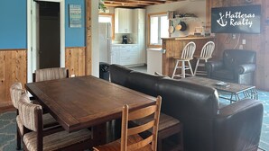 Un coin repas accueillant avec une table et des chaises en bois, un banc en cuir et une cuisine visible au fond.