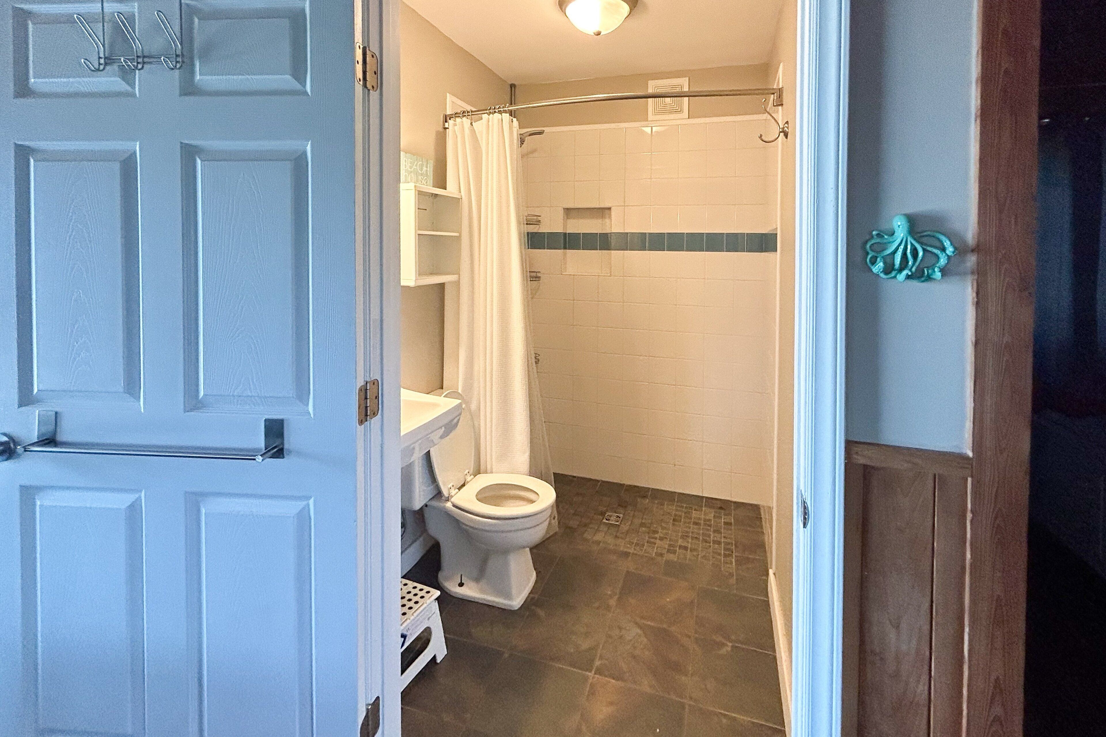 Une salle de bain équipée de toilettes, d’une douche et d’une porte sur laquelle est fixé un porte-serviettes.
