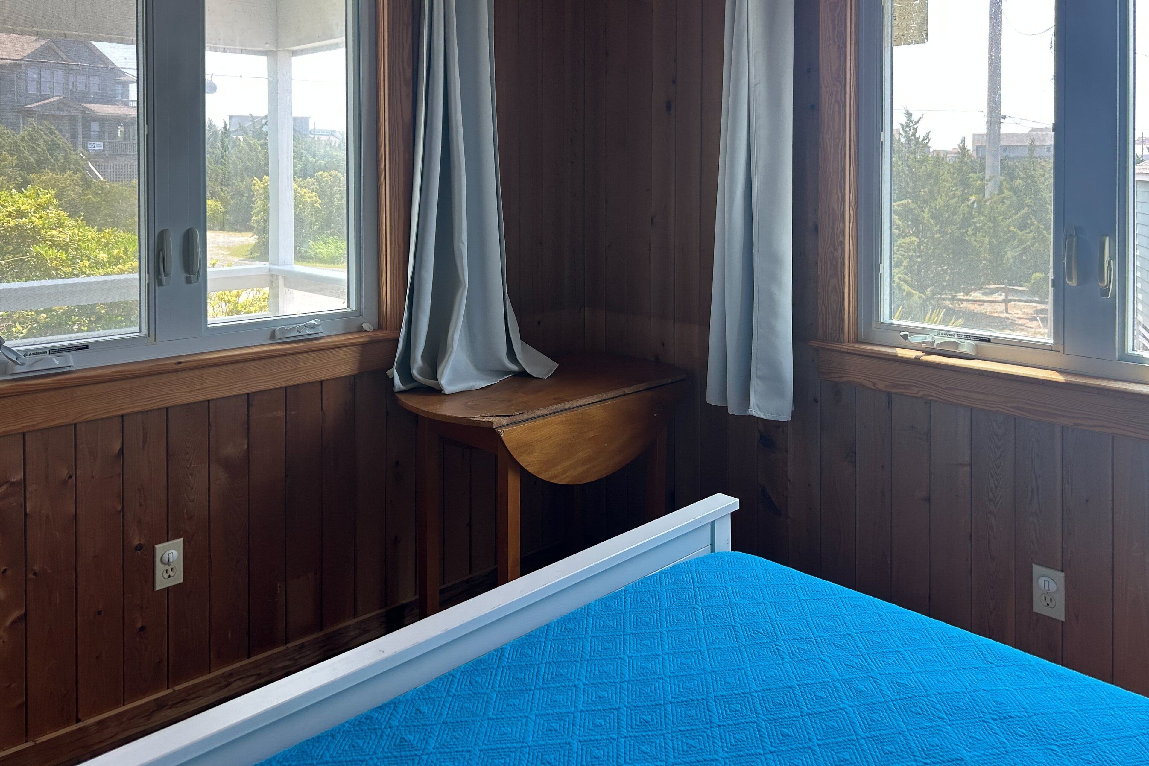 A room with wooden walls, a blue bed, and a window with curtains.