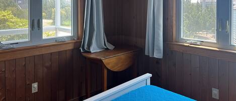 A room with wooden walls, a blue bed, and a window with curtains.
