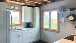 Une cuisine moderne avec des meubles blancs, un four encastré et une fenêtre donnant sur un paysage verdoyant.