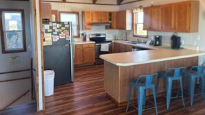 A kitchen with wooden cabinets, a central island with bar stools, a refrigerator, and a stove. - Sand Dollar #13-HC: Oceanfront, Dog-Friendly, Private Hot Tub (Avon)