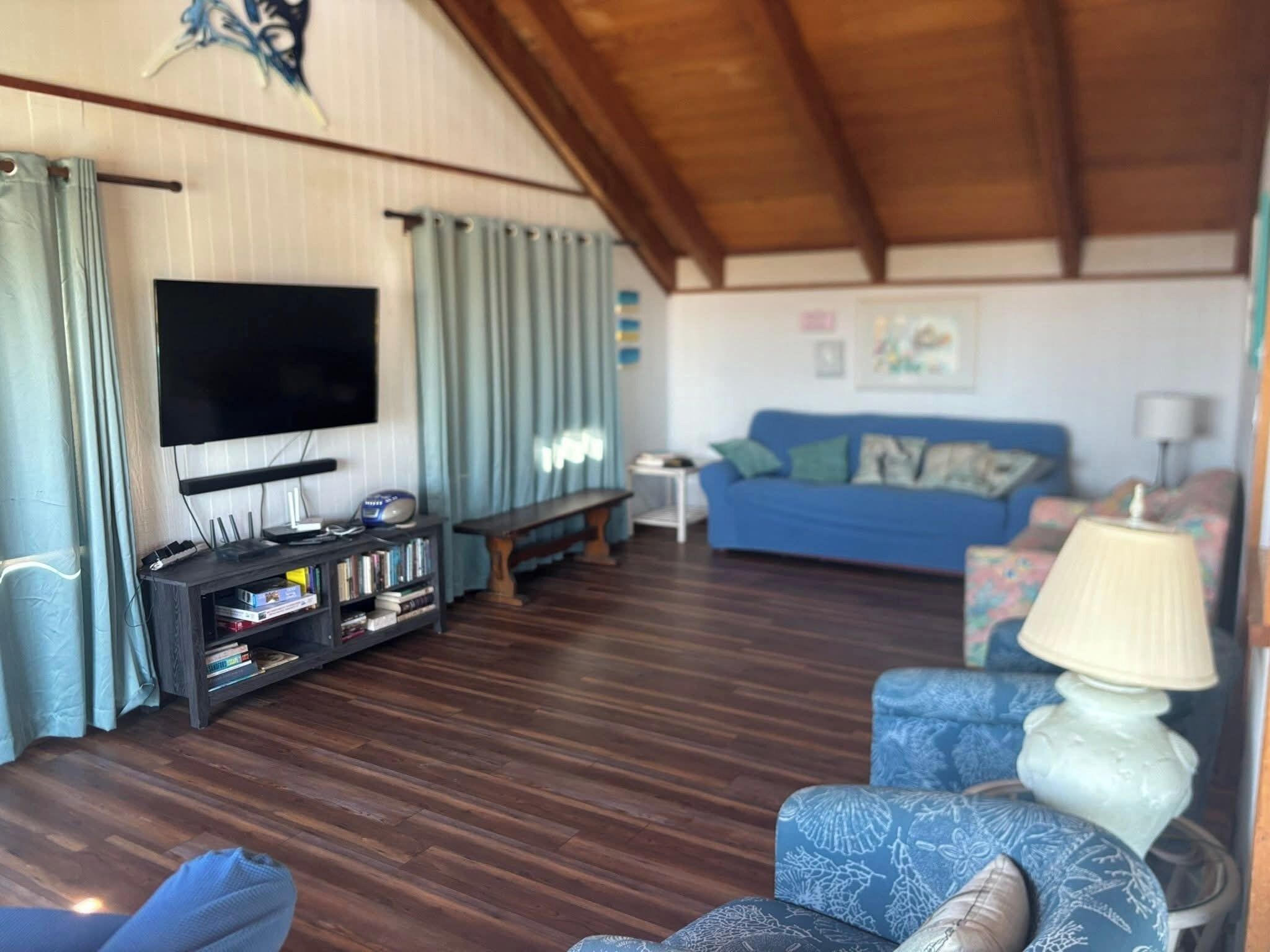 Una sala de estar con televisor de pantalla plana, una estantería, un sofá azul y un sillón estampado.